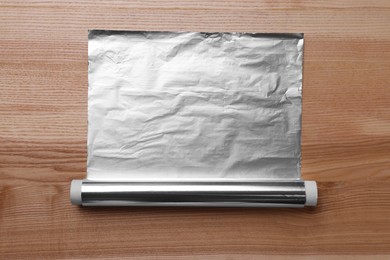 Roll of aluminum foil on wooden table, top view