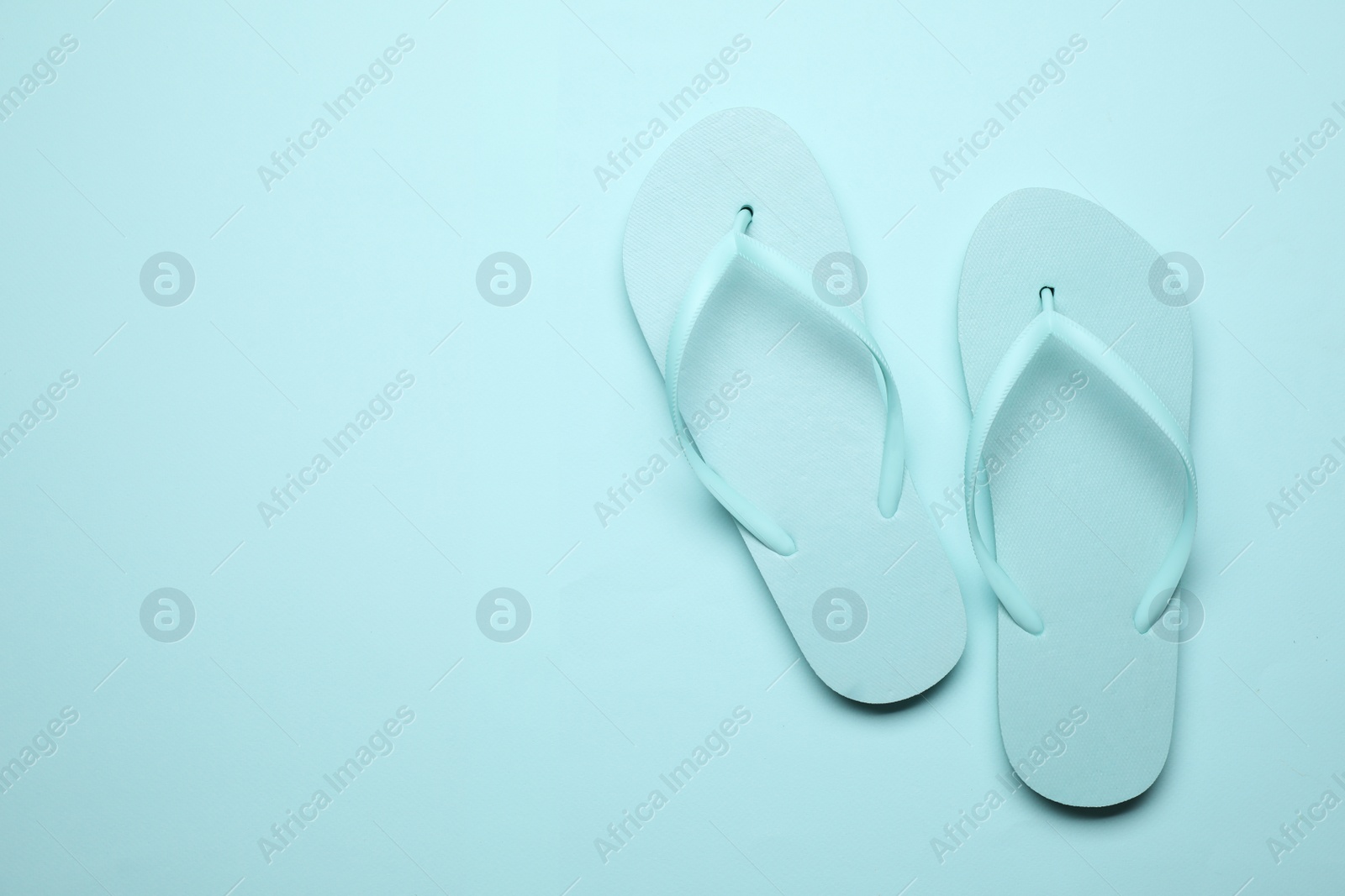 Photo of Pair of stylish flip flops on light blue background, top view with space for text. Beach objects