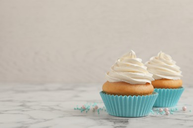 Photo of Delicious cupcakes decorated with cream on white marble table, space for text