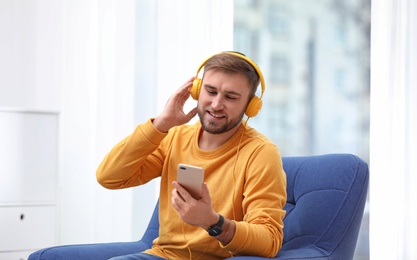 Photo of Young man with headphones and mobile device sitting in armchair at home
