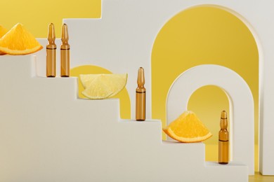Photo of Stylish presentation of skincare ampoules with vitamin C and citrus slices on decorative stairs against yellow background, closeup
