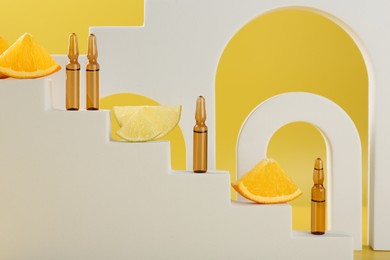 Stylish presentation of skincare ampoules with vitamin C and citrus slices on decorative stairs against yellow background, closeup