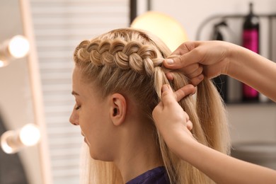 Photo of Professional stylist braiding client's hair in salon