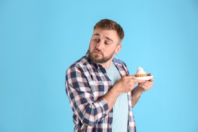 Photo of Greedy young man hiding cupcake on light blue background