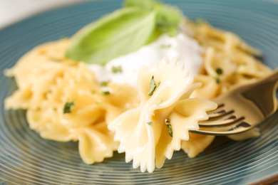 Photo of Tasty farfalle pasta with herbs on fork, closeup