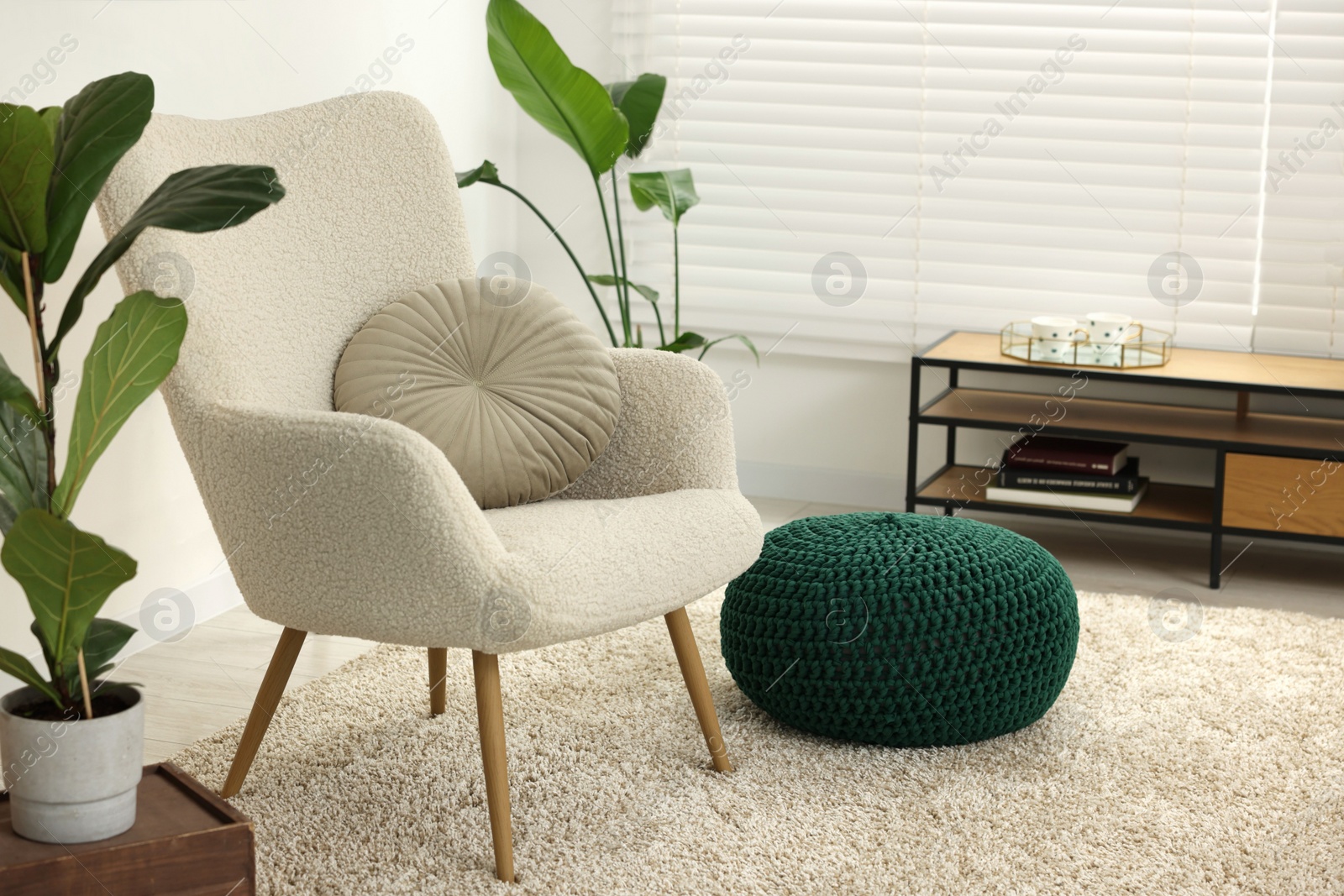 Photo of Comfortable armchair, pouf and houseplants in living room. Interior design