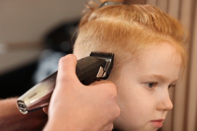 Professional hairdresser cutting boy's hair in beauty salon, closeup