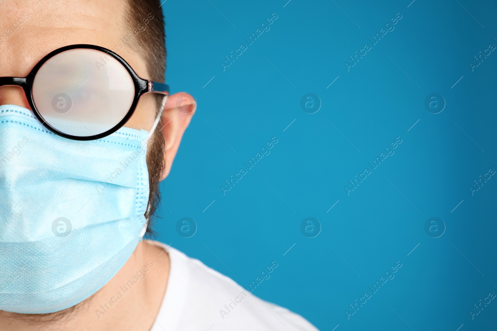 Photo of Man with foggy glasses caused by wearing disposable mask on blue background, space for text. Protective measure during coronavirus pandemic