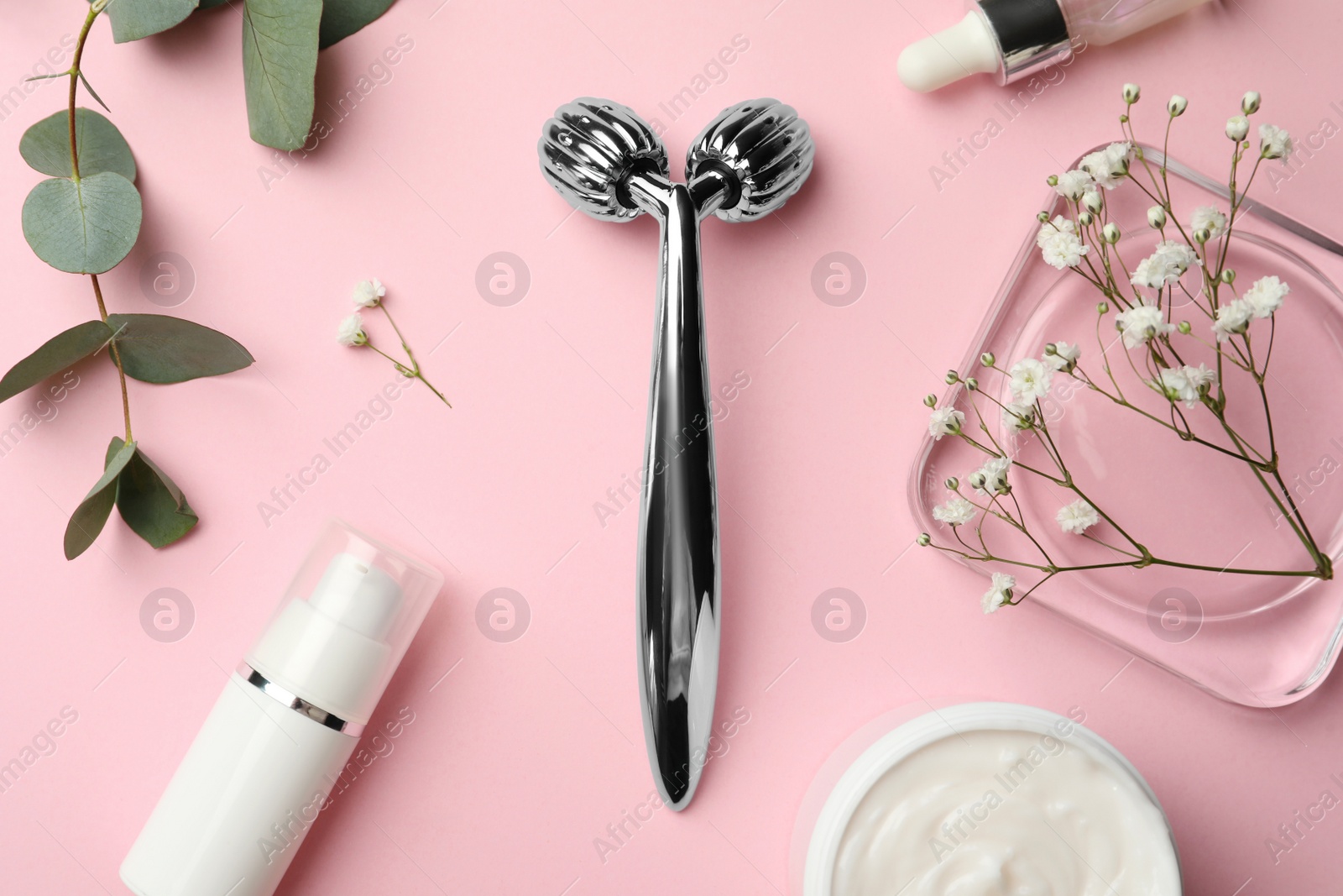 Photo of Metal face roller, cosmetic products and flowers on pink background, flat lay