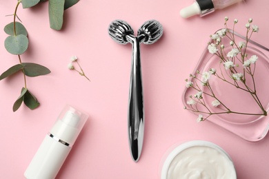 Photo of Metal face roller, cosmetic products and flowers on pink background, flat lay