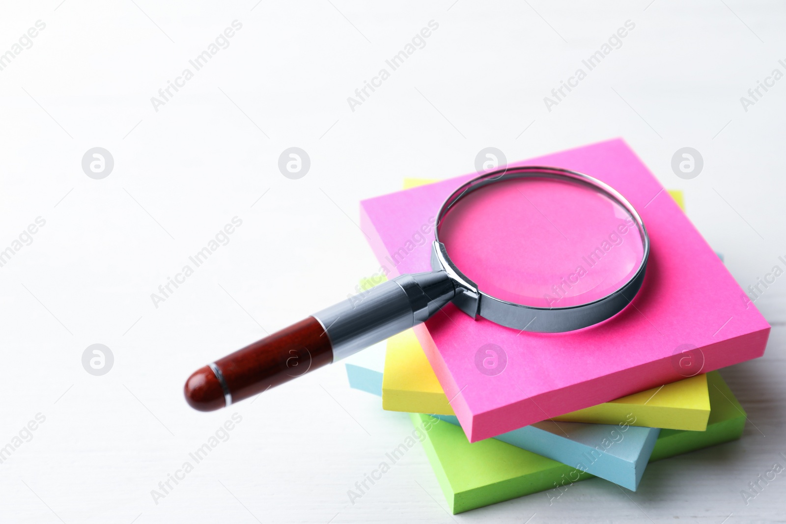 Photo of Magnifier glass and stack of colorful memory stickers on white wooden table, closeup. Find keywords concept