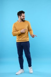 Photo of Happy young man pointing at something on light blue background