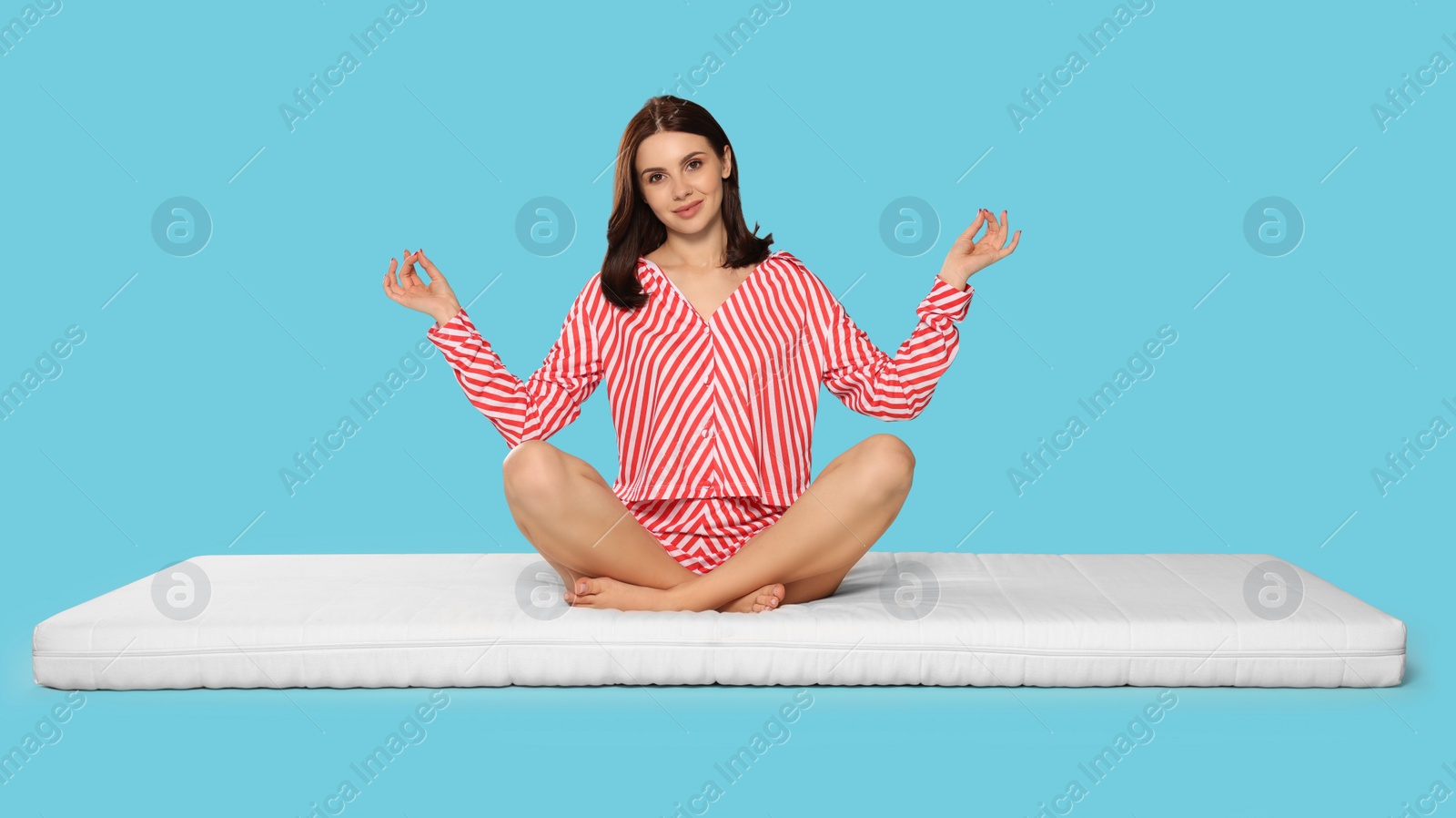 Photo of Young woman meditating on soft mattress against light blue background