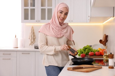 Photo of Muslim woman cooking delicious dish with vegetables on cooktop in kitchen