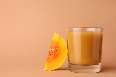 Tasty pumpkin juice in glass and cut pumpkin on pale orange background. Space for text