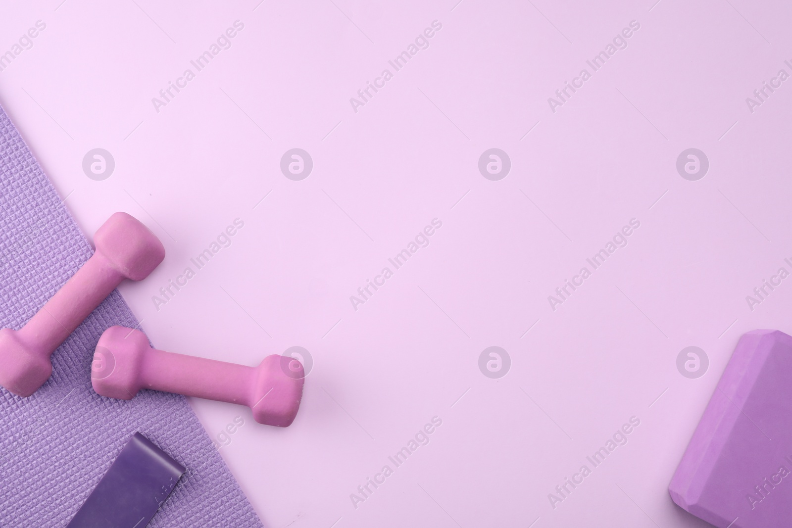 Photo of Two dumbbells, yoga block, mat and fitness elastic band on violet background, flat lay. Space for text