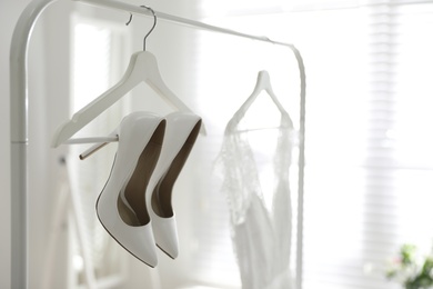 Photo of Pair of white high heel shoes and wedding dress on clothing rack indoors. Space for text