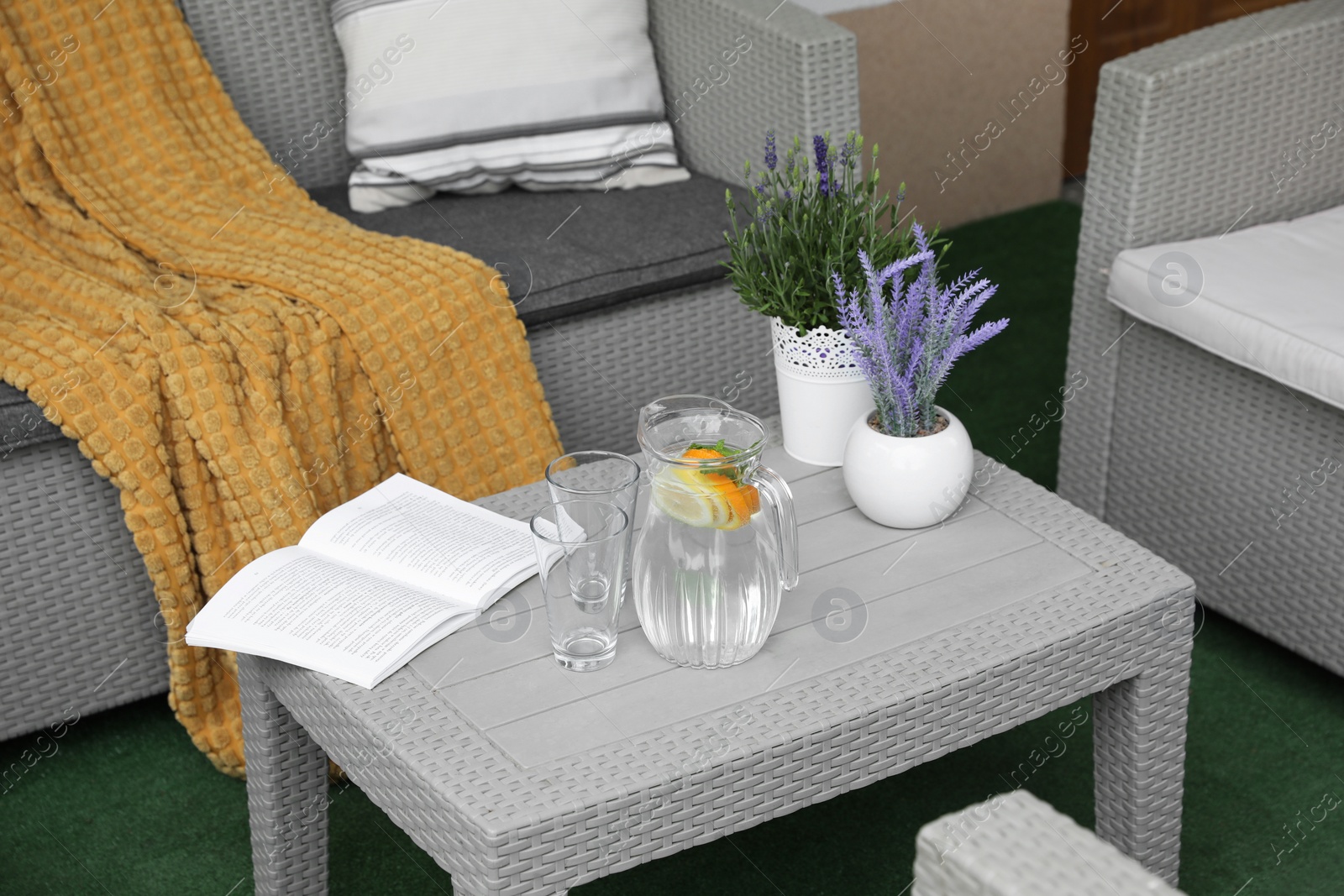 Photo of Table with book, jug of water and potted plants in front of sofa on outdoor terrace