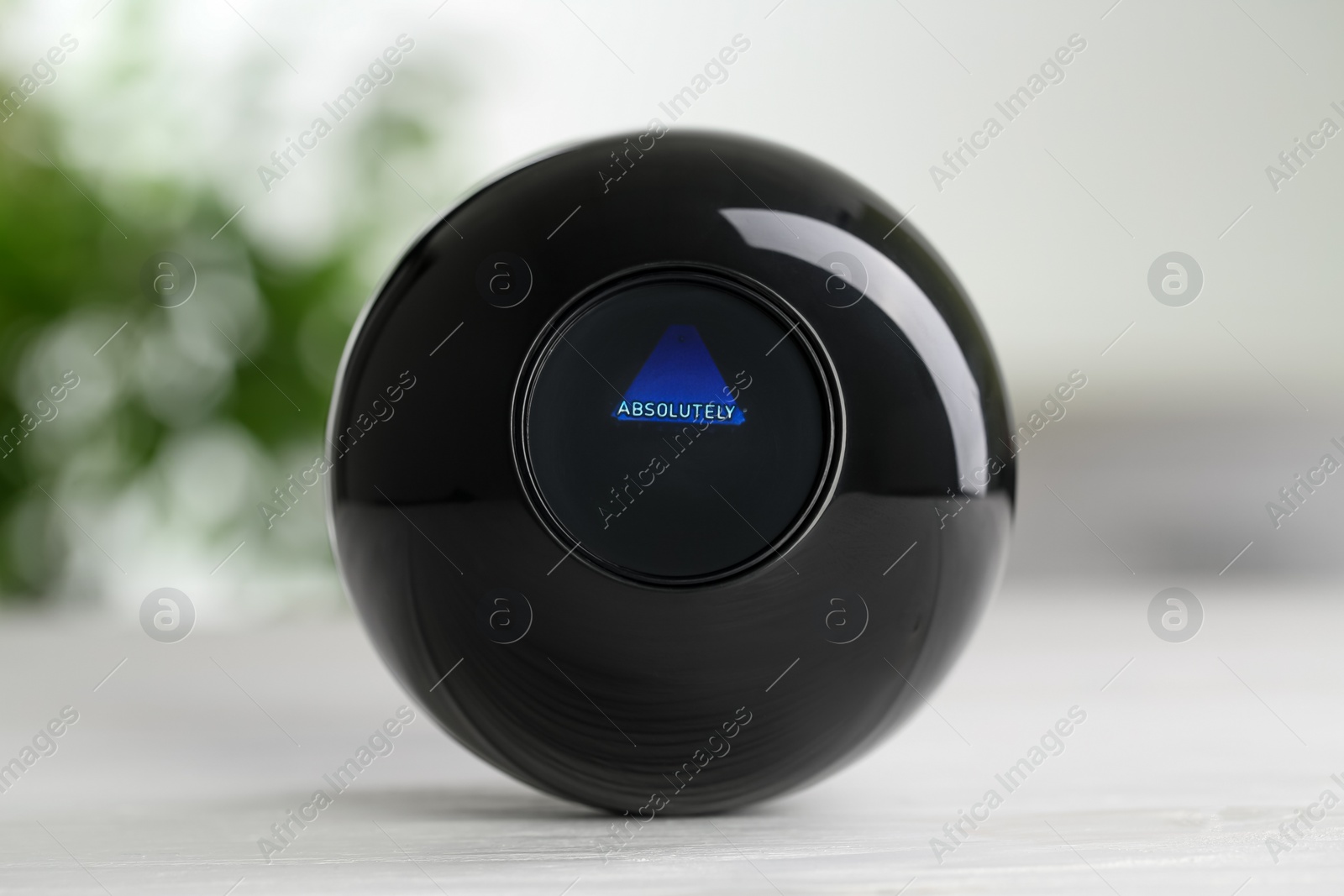 Photo of Magic eight ball with prediction Absolutely on light wooden table, closeup