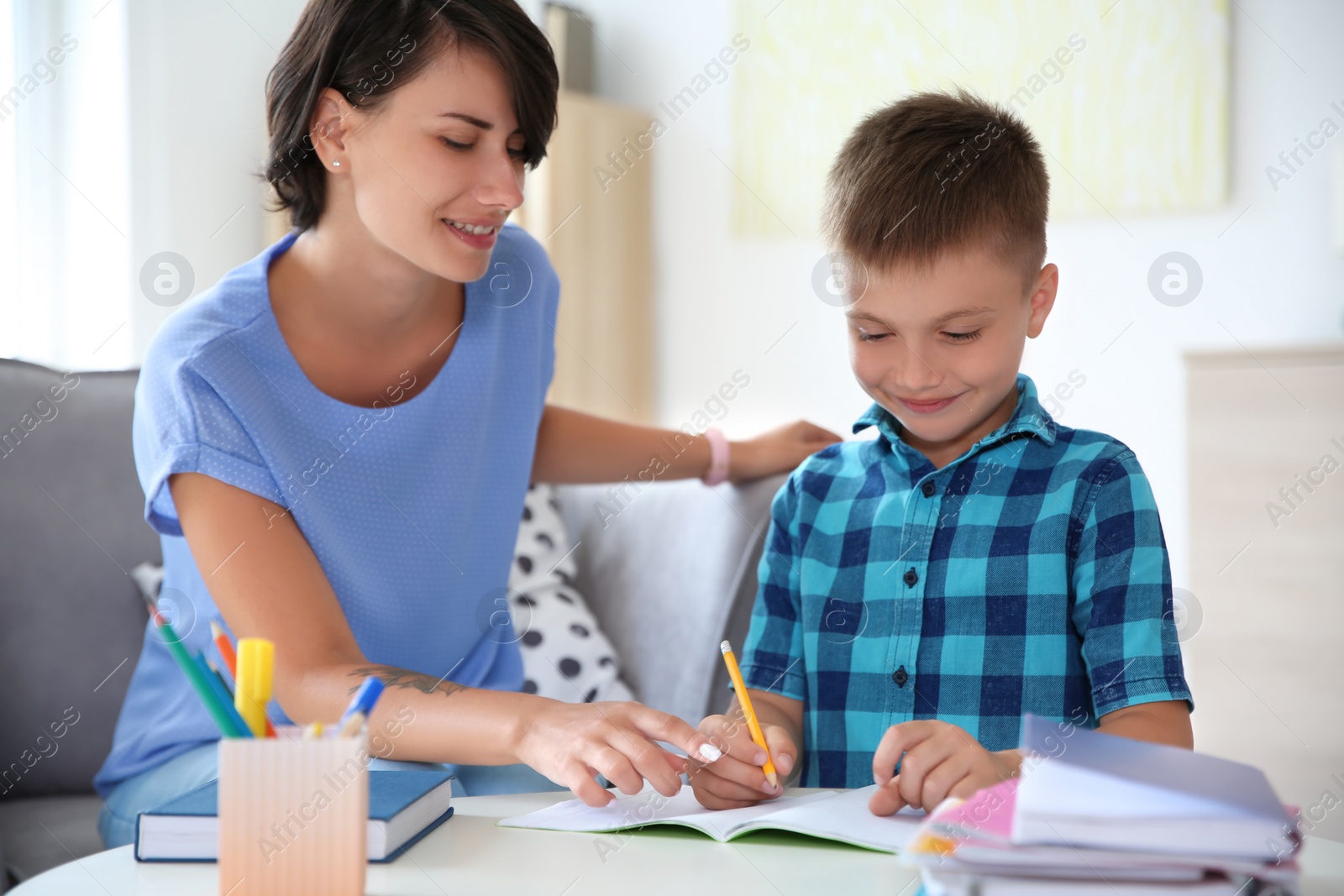 Photo of Young woman helping her child with homework at home. Elementary school