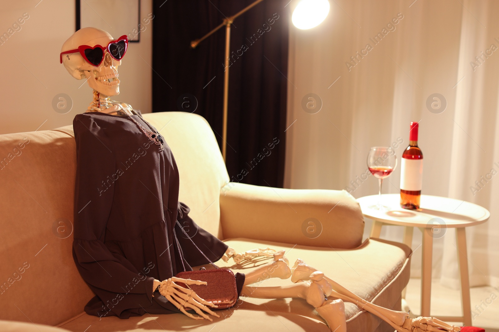 Photo of Skeleton in dress sitting on sofa at home