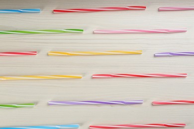 Colorful plastic drinking straws on white wooden table, flat lay