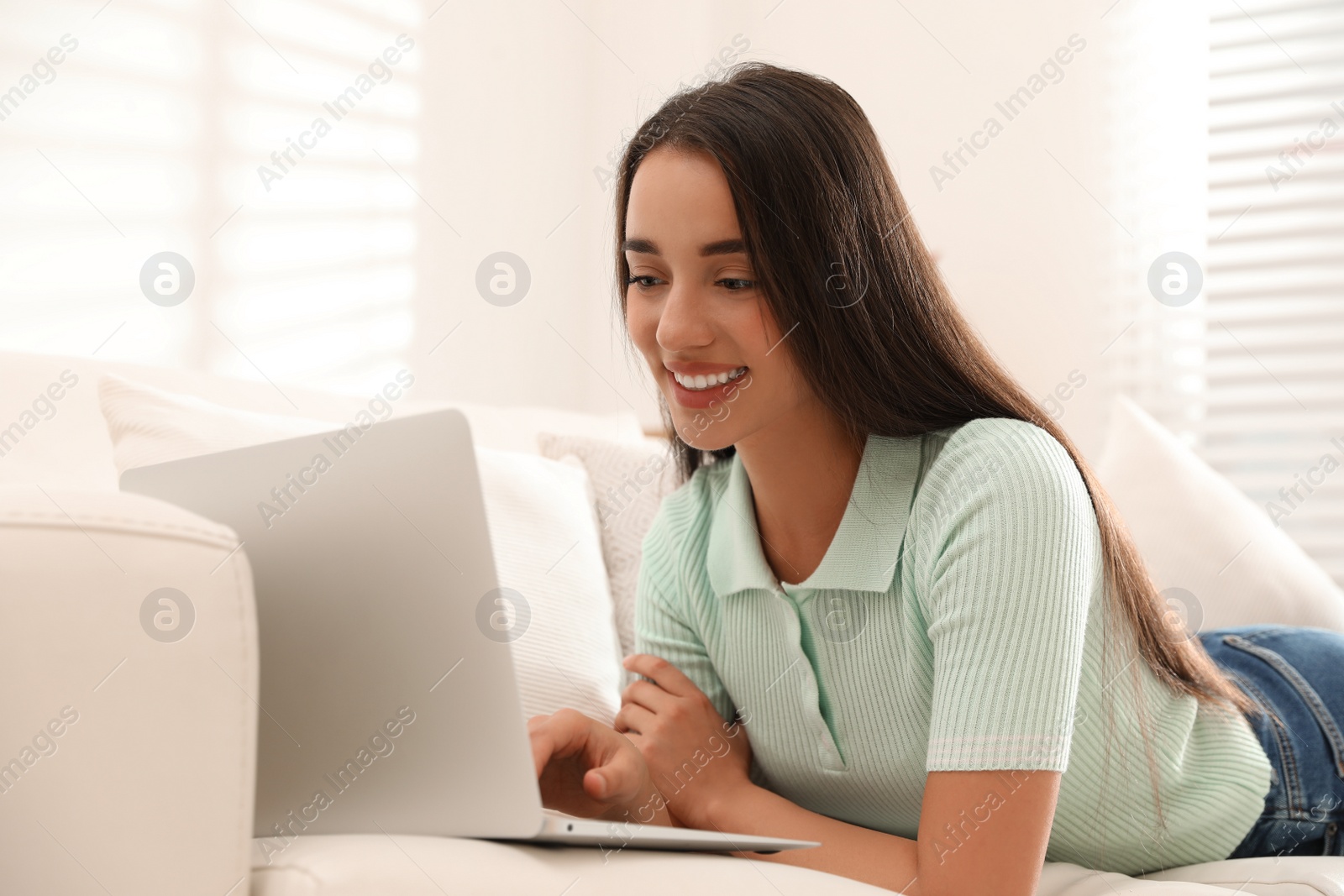 Photo of Young woman using laptop for search on sofa at home