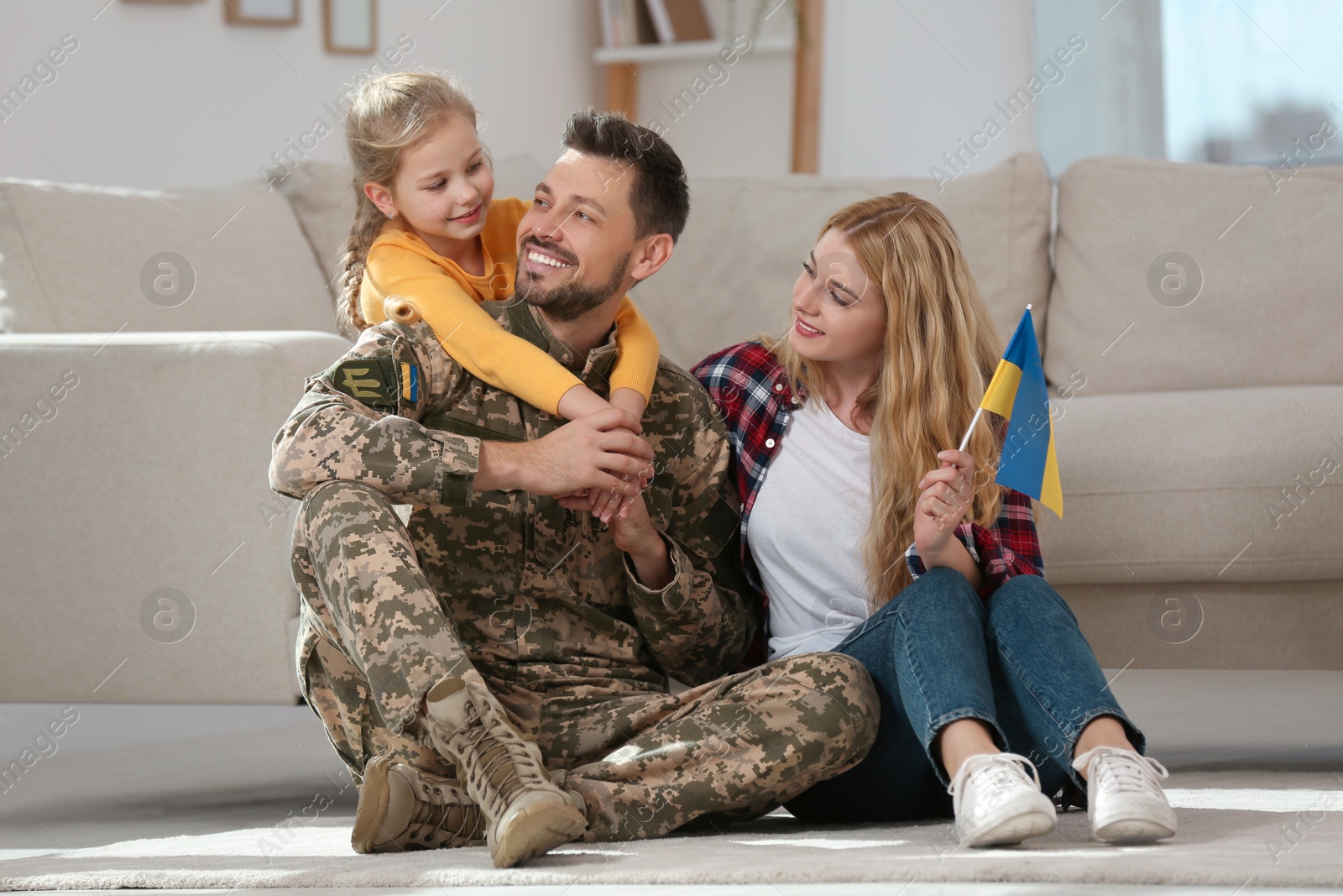 Photo of Soldier in military uniform reunited with his family and Ukrainian flag on floor at home