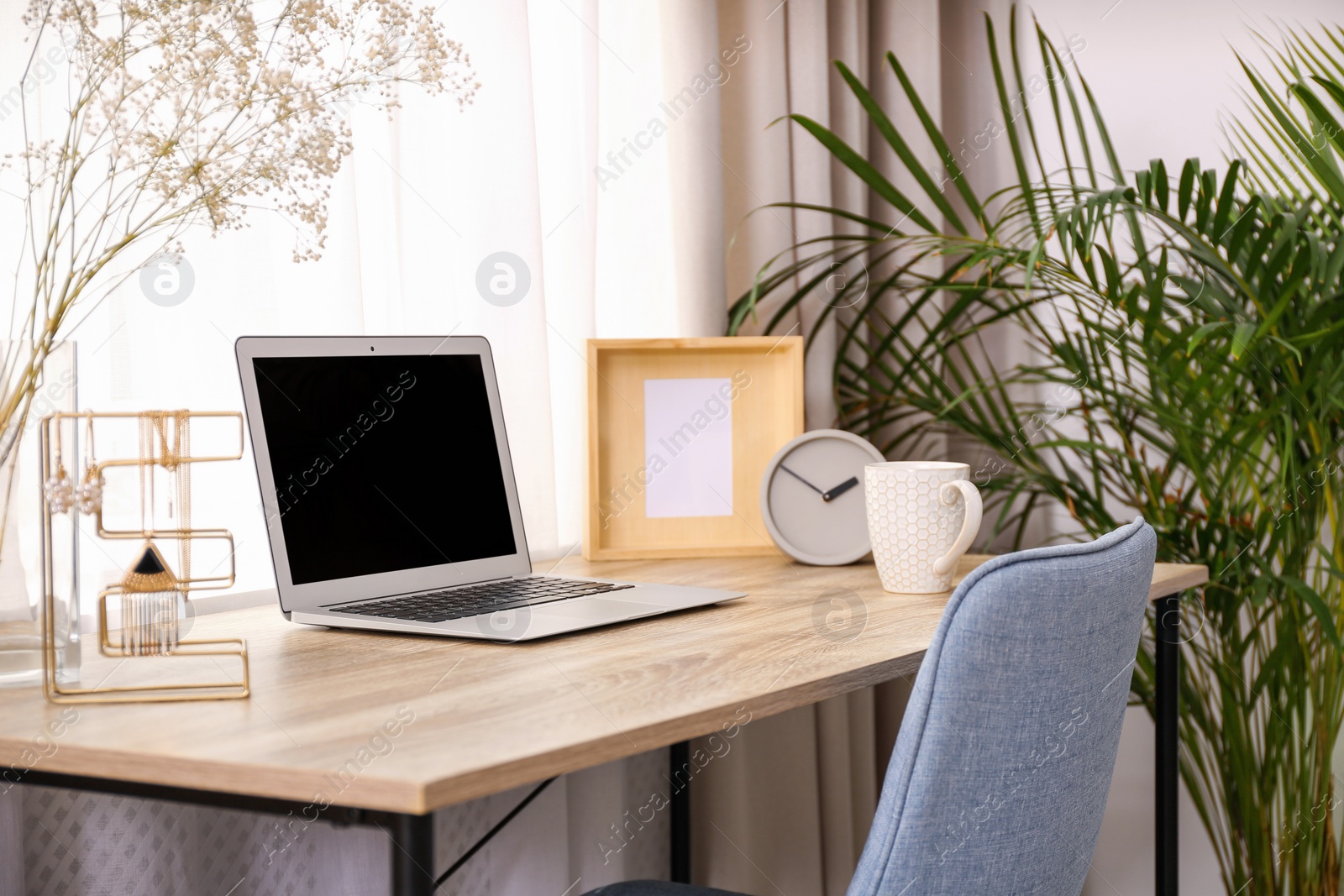 Photo of Stylish workplace interior with laptop on wooden table near window