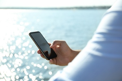 Photo of Man using modern mobile phone near river, closeup