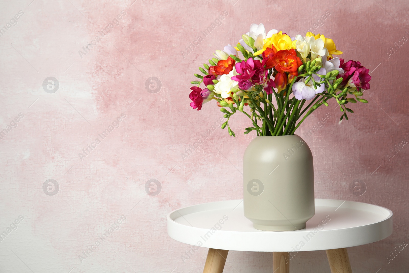 Photo of Bouquet of spring freesia flowers in vase on table against color background, space for text