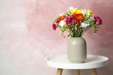 Photo of Bouquet of spring freesia flowers in vase on table against color background, space for text