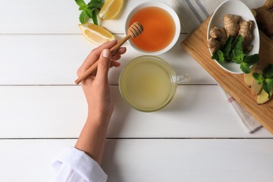Woman drinking delicious ginger tea with honey at white wooden table, top view