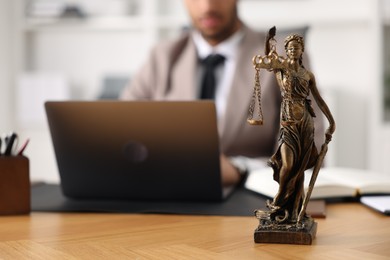 Lawyer working with laptop at table in office, focus on statue of Lady Justice