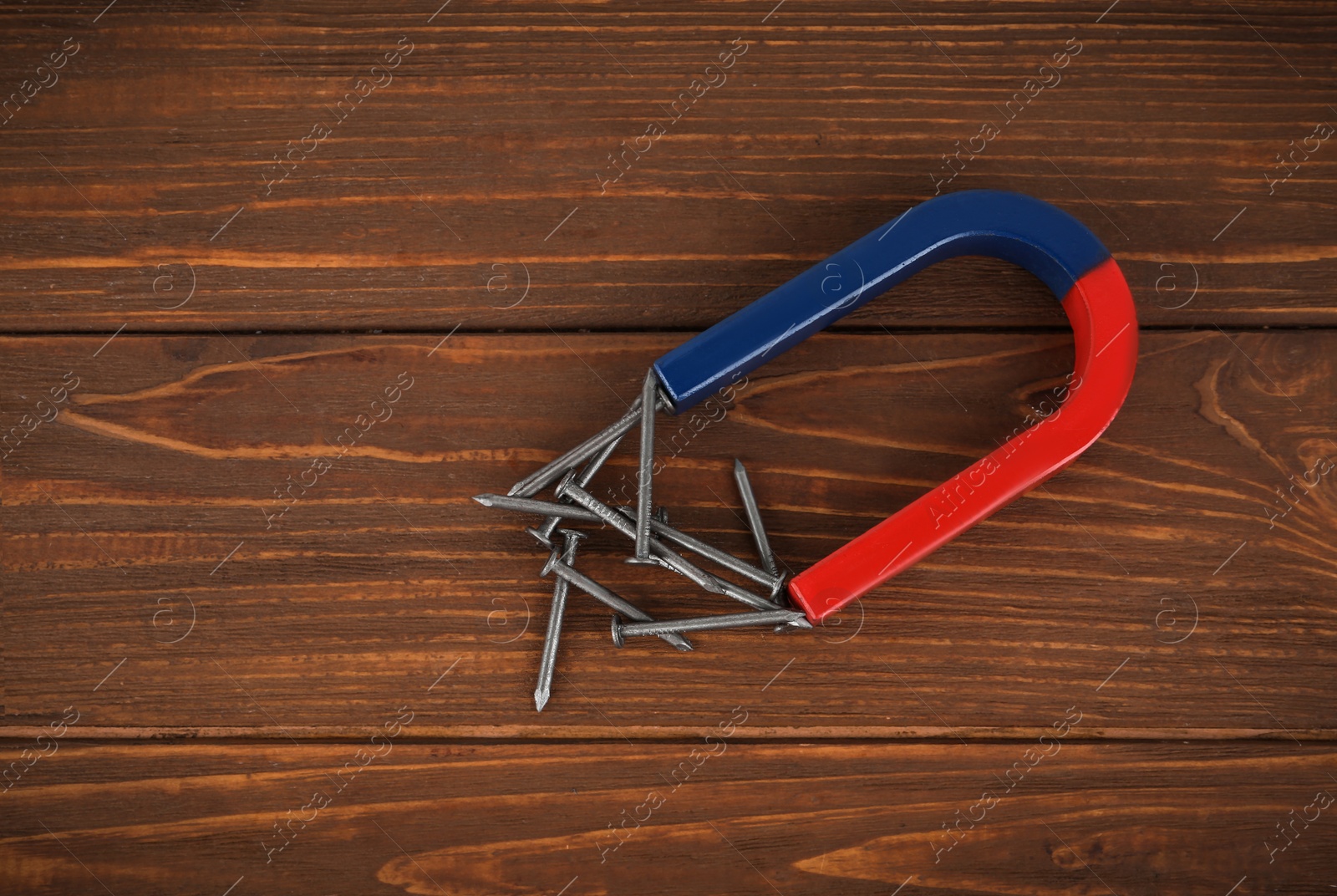 Photo of Horseshoe magnet attracting nails on wooden table, flat lay