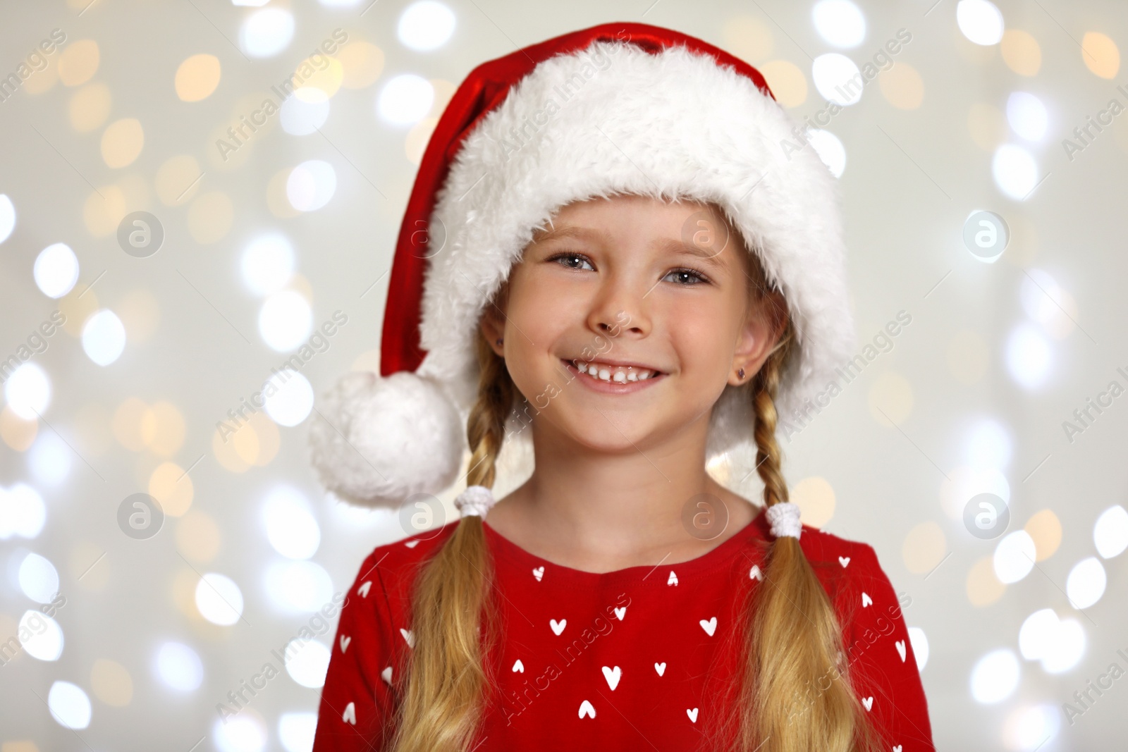 Photo of Happy little child in Santa hat against blurred festive lights. Christmas celebration