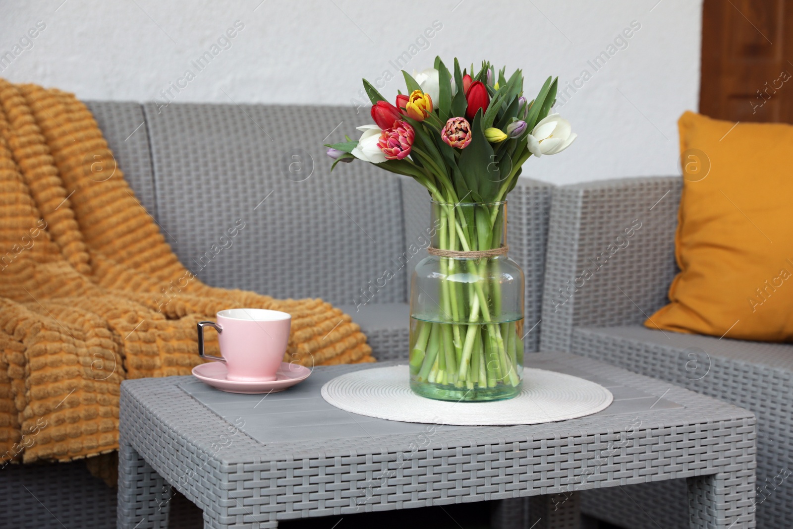 Photo of Beautiful bouquet of colorful tulips and cup with drink on rattan garden table