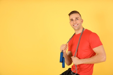 Portrait of young sportive man with jump rope on color background. Space for text