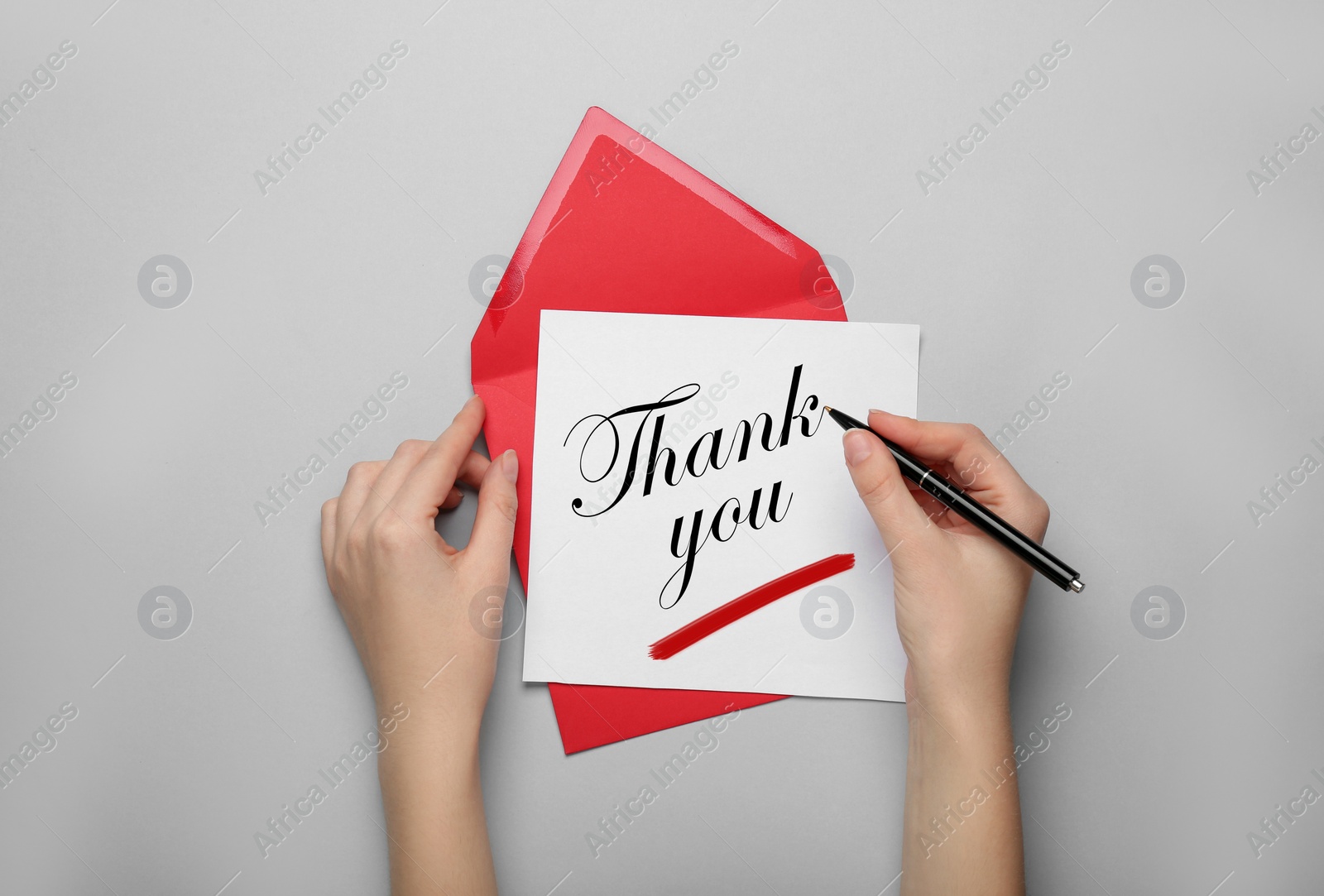 Image of Woman with envelope and card writing phrase Thank You on light grey background, top view