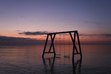 Photo of Picturesque view of swing in water on sunrise