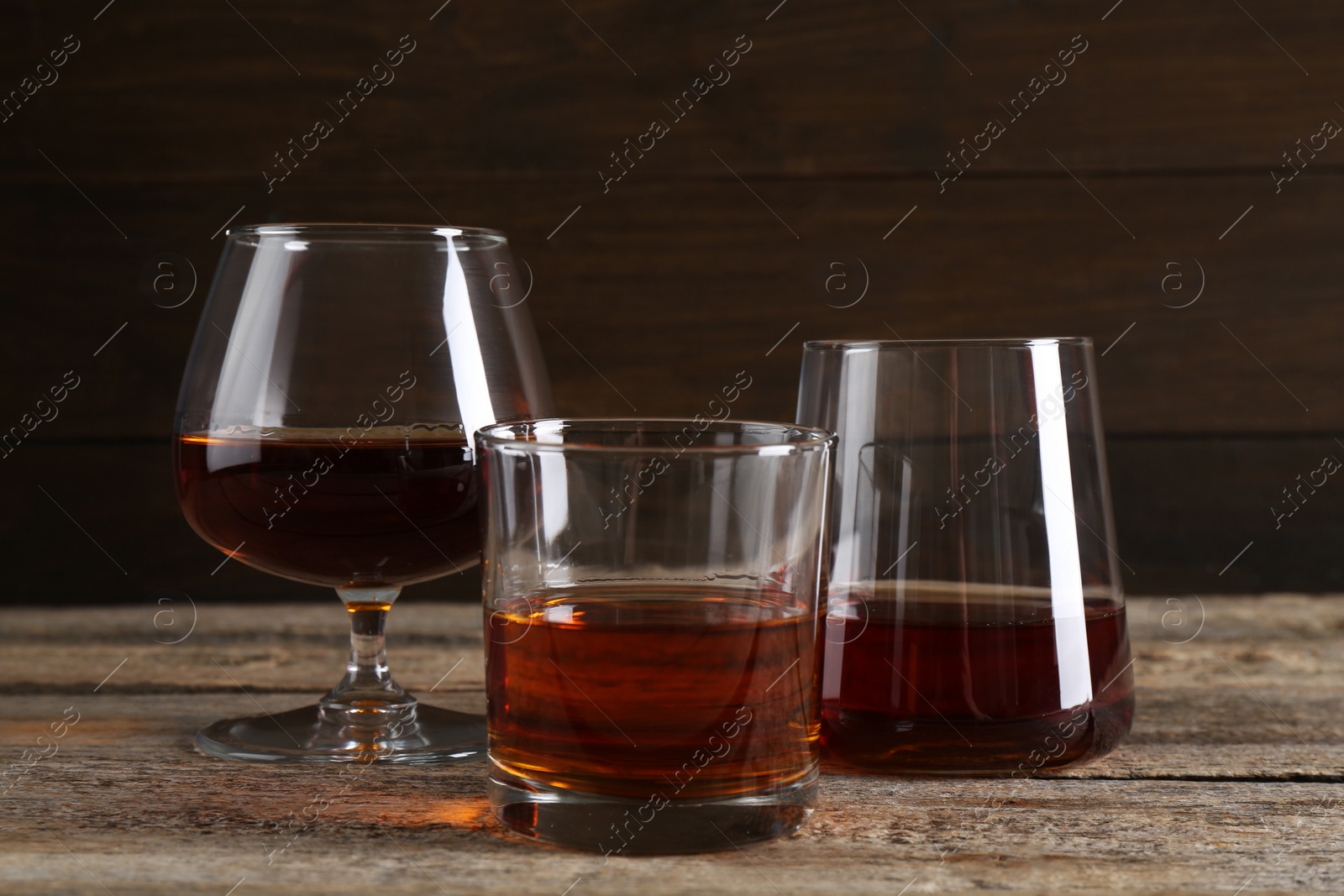 Photo of Different delicious liqueurs in glasses on wooden table
