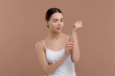 Woman with dry skin checking her arm on beige background