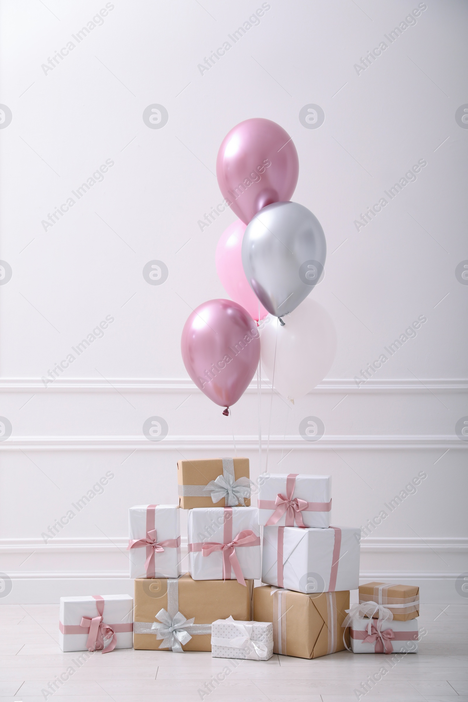 Photo of Many gift boxes and balloons near white wall in room