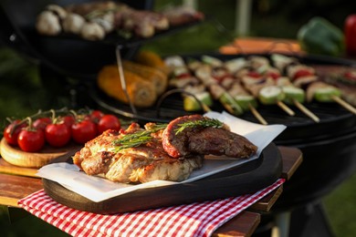 Photo of Tasty cooked meat and cherry tomatoes on table near barbecue grill outdoors