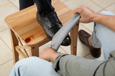 Photo of Man shining client's shoe on wooden stool indoors, closeup