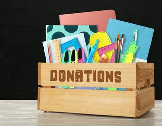 Image of Donation box with different school stationery on white wooden table near blackboard