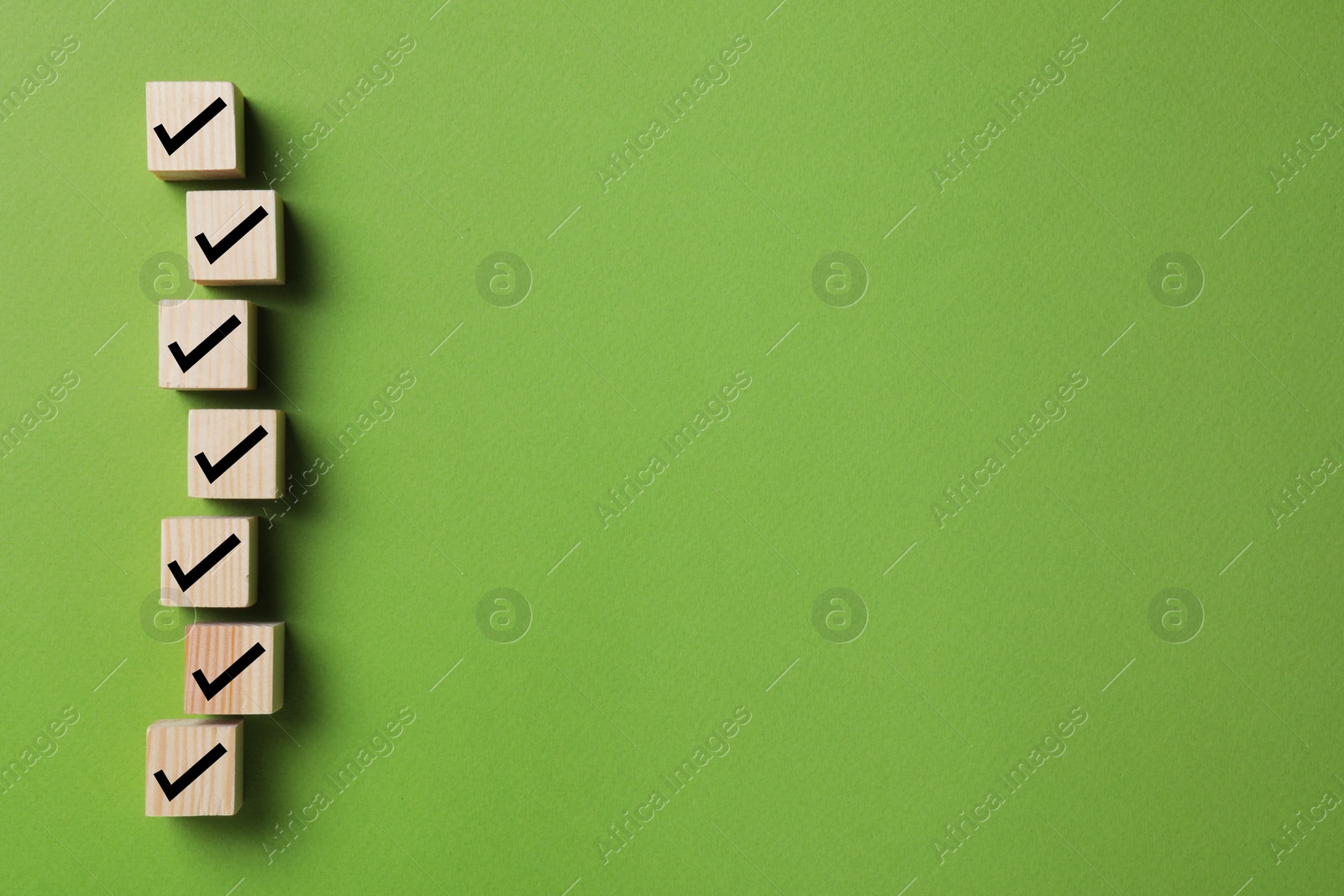 Image of Wooden cubes with check marks on green background, flat lay. Space for text