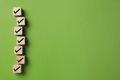 Wooden cubes with check marks on green background, flat lay. Space for text