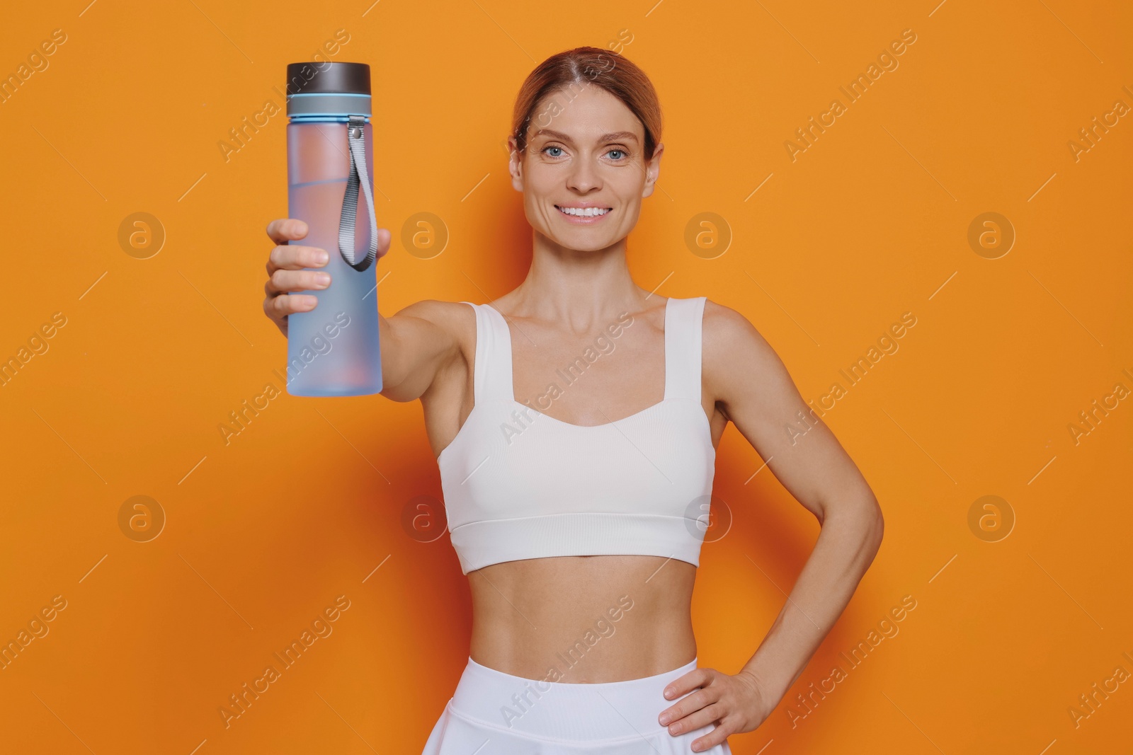 Photo of Sportswoman with bottle of water on orange background