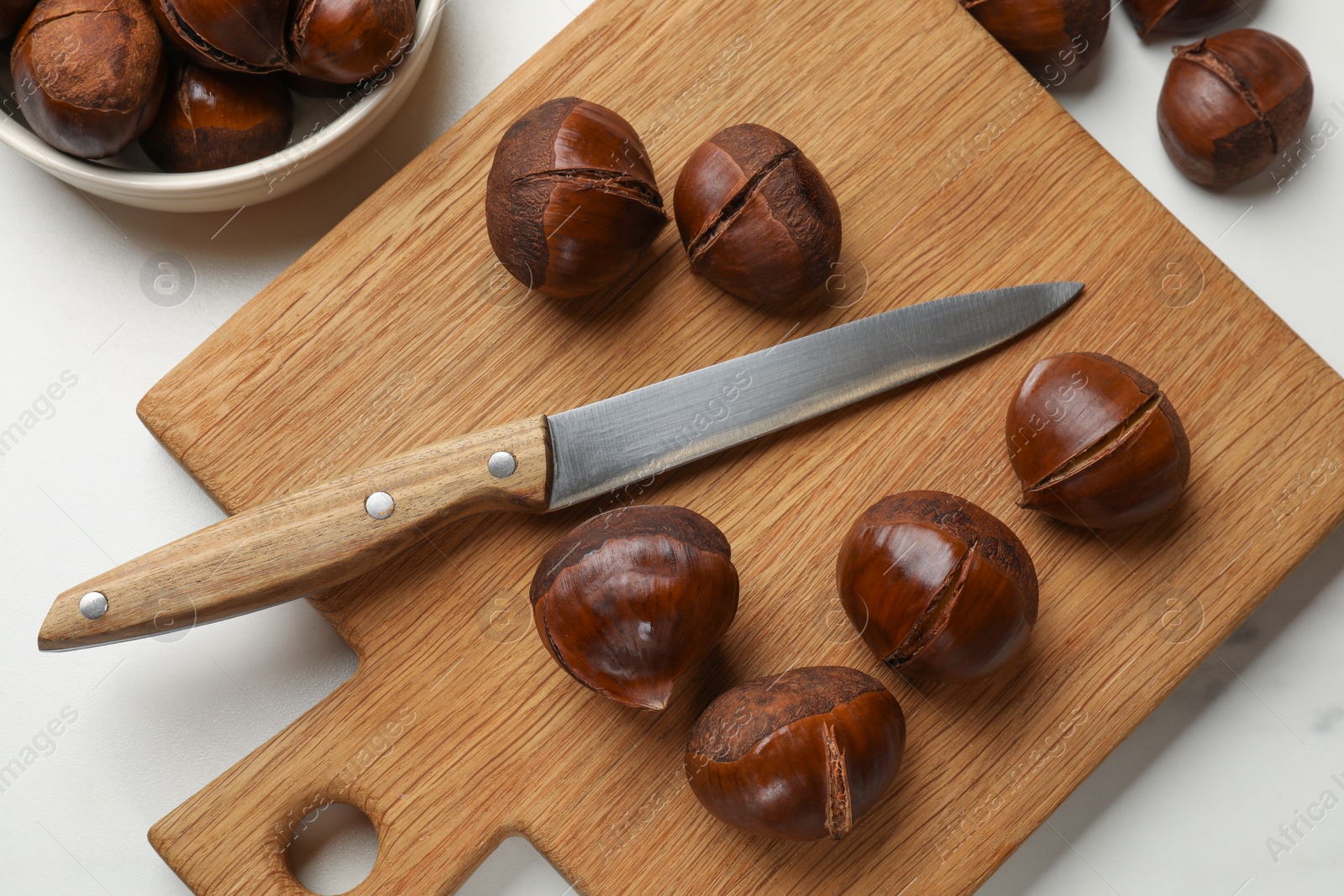 Photo of Roasted edible sweet chestnuts and knife on white table, flat lay